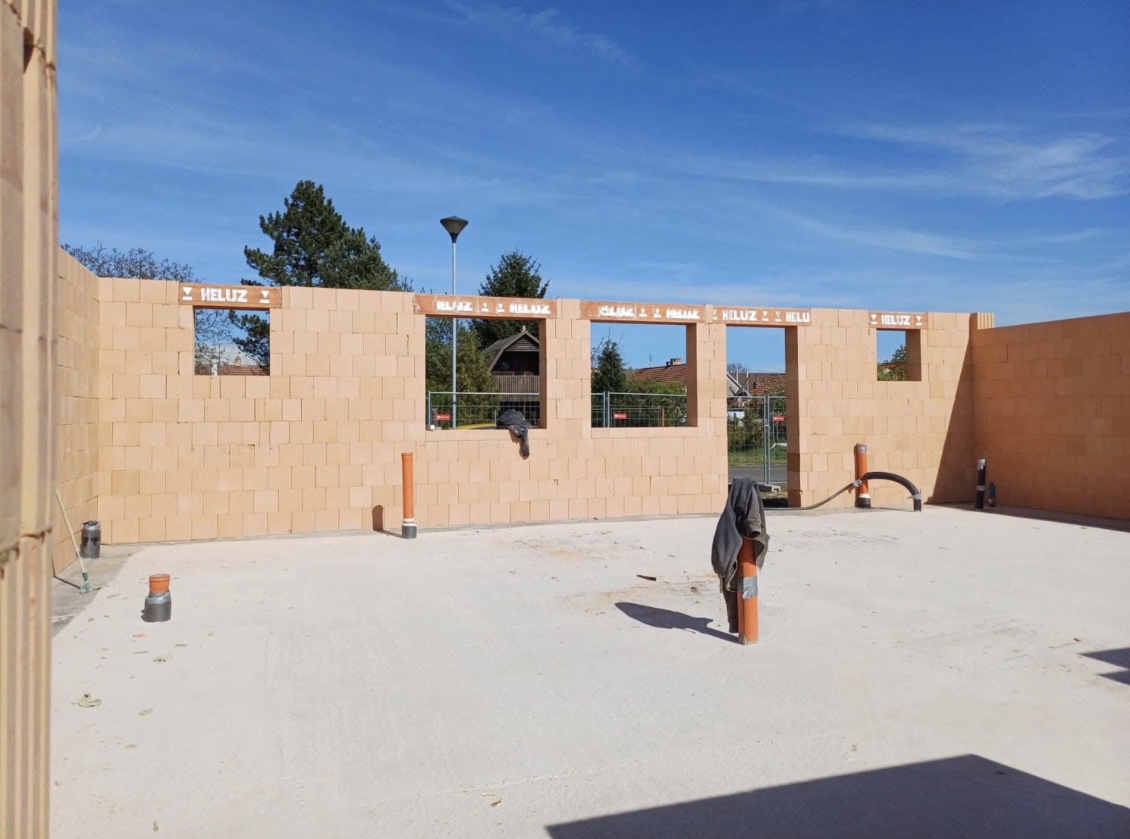 Stavba rodinného domu z tvárnic, otevřené průchody a okna, betonová podlaha, modrá obloha.